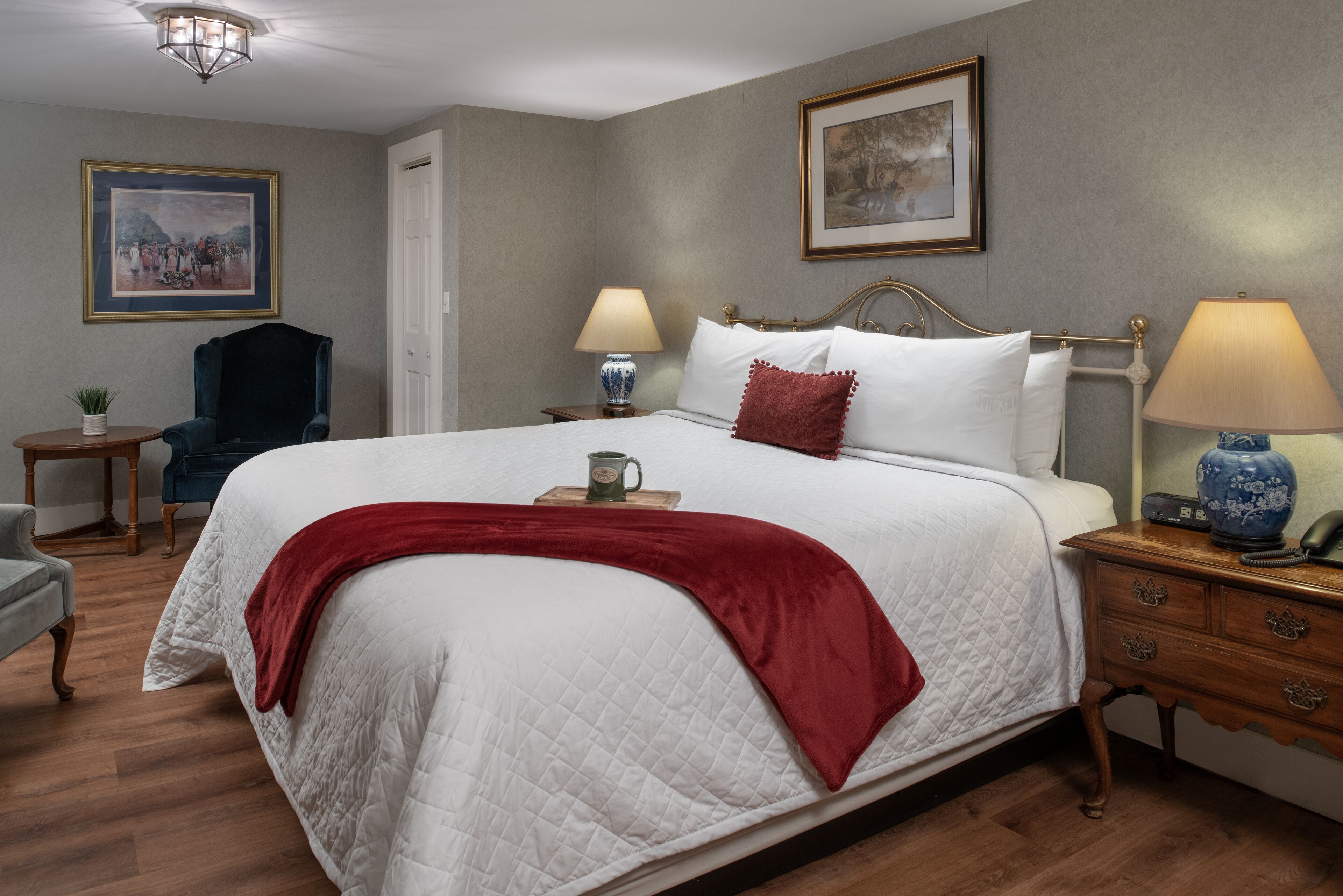 Habitación de hotel ordenada y bien cuidada, con una cama grande, dos mesitas de noche, una silla y un cuadro en la pared.