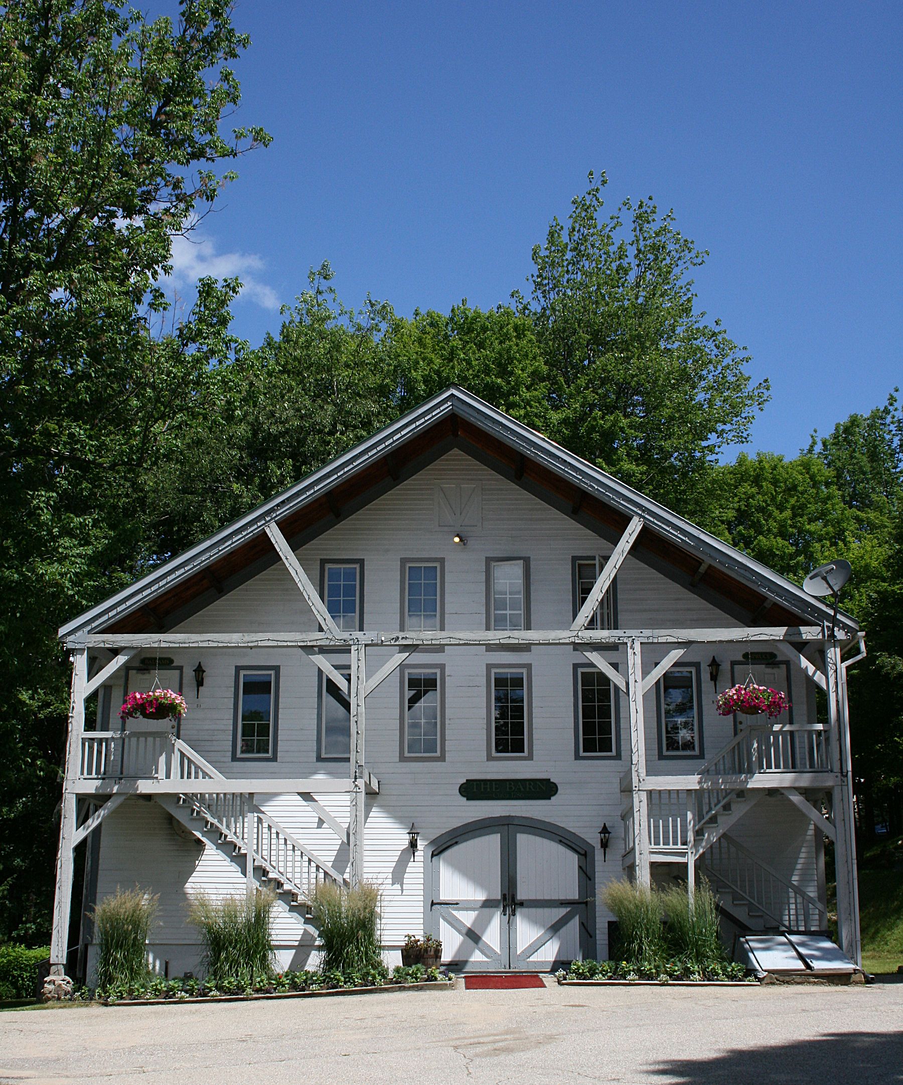A white two-story building with a central entrance, a porch with railings, and a staircase leading to the second floor.