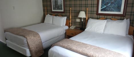 Una camera d'albergo con due letti singoli, un comodino con una lampada e due quadri appesi al muro.