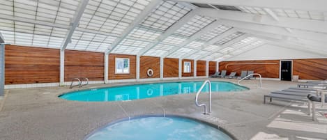 An indoor swimming pool with two separate pools, wooden panel walls, and a high ceiling with skylights.