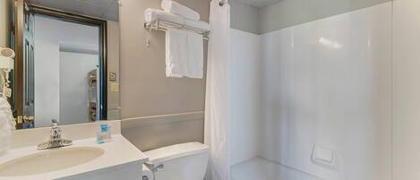 A bathroom with a toilet, sink, mirror, towel rack, and shower curtain.