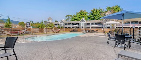 A pool area with lounge chairs and tables, surrounded by wooden fences and a building with multiple balconies.