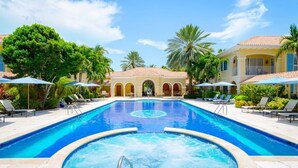 Una piscina amb gandules i ombrelles, envoltada de palmeres i un edifici amb arcs.