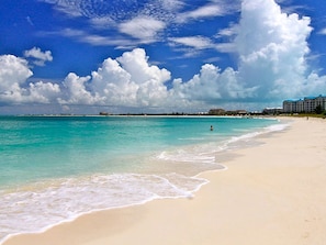 A beach with clear turquoise water, a sandy shore, and a distant building complex. - Villa Renaissance (Providenciales)