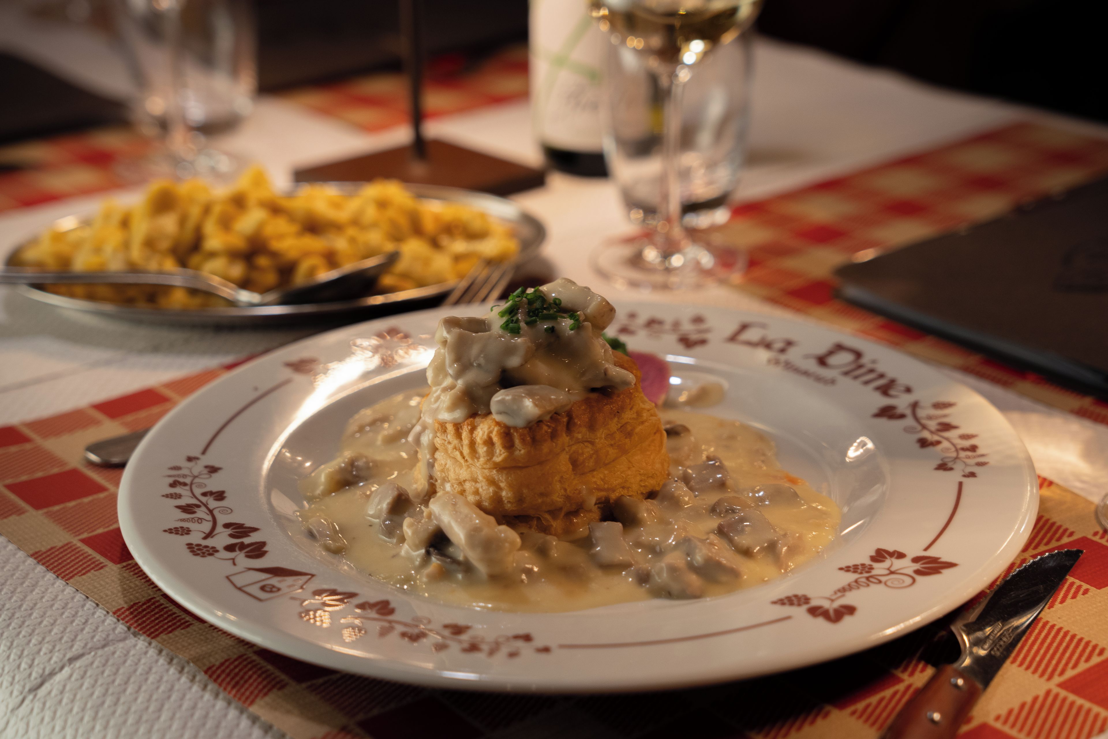 A plate of food with a creamy sauce and a biscuit on a table with a checkered tablecloth.