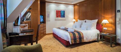 A hotel room with a bed, a desk, a chair, a TV, and a painting on the wall.
