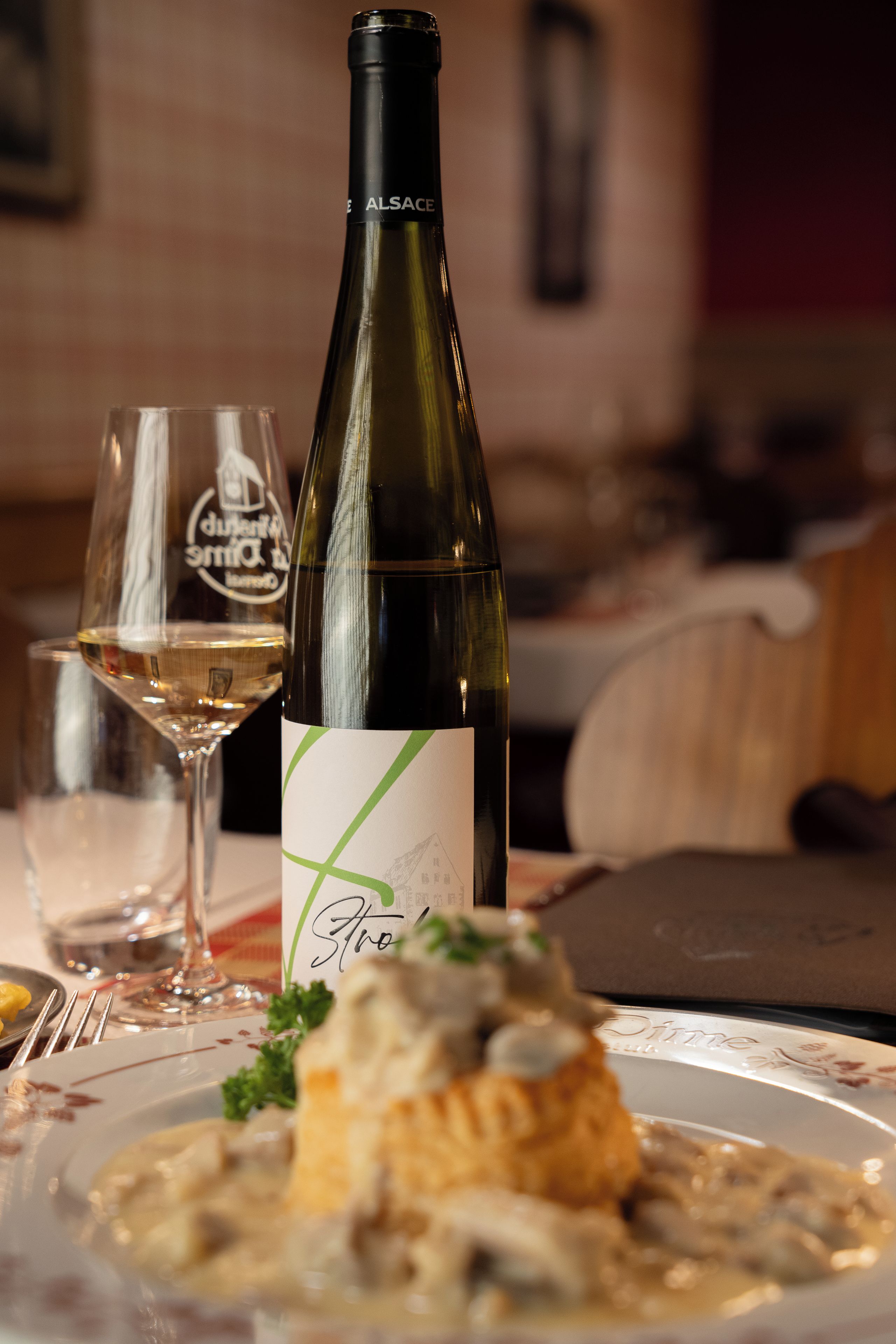 A bottle of wine, a glass of white wine, and a plate with food on a table.