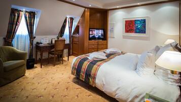 A hotel room with a bed, a desk, a chair, a television, and a painting on the wall.