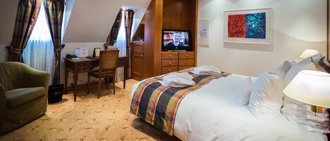 Une chambre d’hôtel avec un lit, un bureau, une chaise, une télévision et un tableau au mur.