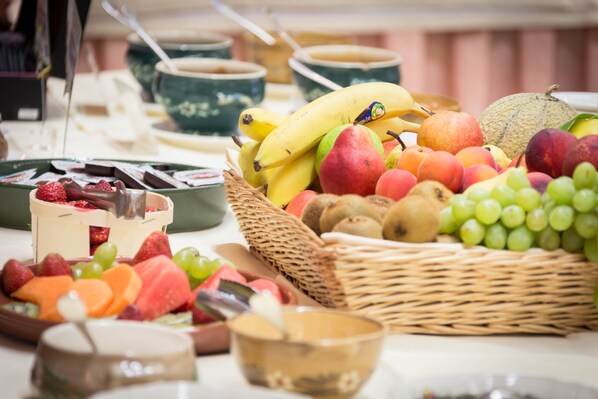 Una mesa con diversas frutas y postres, como plátanos, manzanas, uvas y chocolate.