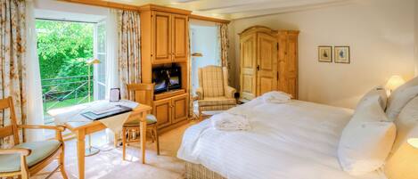 A bedroom with a large bed, a desk with a chair, a television, and a wardrobe.