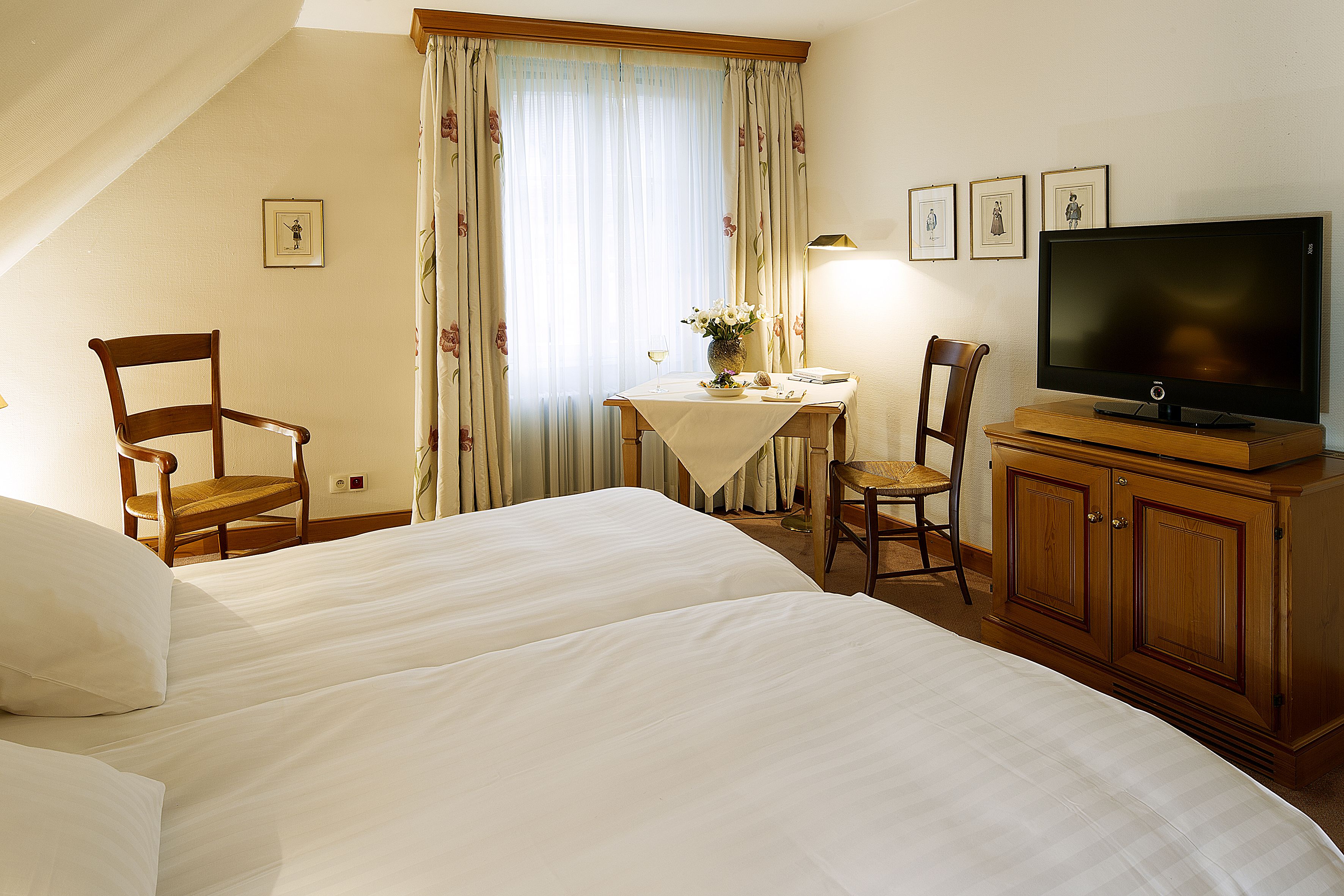 Una habitación de hotel con dos camas, una mesa de comedor con sillas, un televisor y un armario.