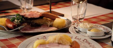 Une table à manger avec des assiettes remplies de nourriture, un verre de vin blanc et un menu.
