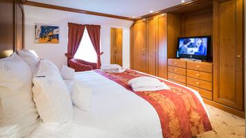 Una habitación de hotel con una cama grande, un televisor sobre un mueble de madera y un ventanal con cortinas.