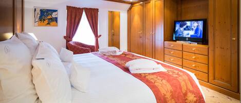 A hotel room with a large bed, a TV on a wooden cabinet, and a window with curtains.