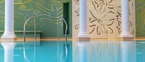 A swimming pool with clear blue water, surrounded by white columns and green walls with gold patterns.