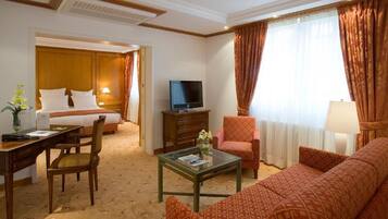 A hotel room with a bed, a TV, a desk, a chair, a sofa, and a coffee table.
