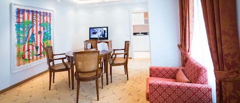 Hotellihuone, jossa on ruokailutila, televisio, sohva ja taulu seinällä.