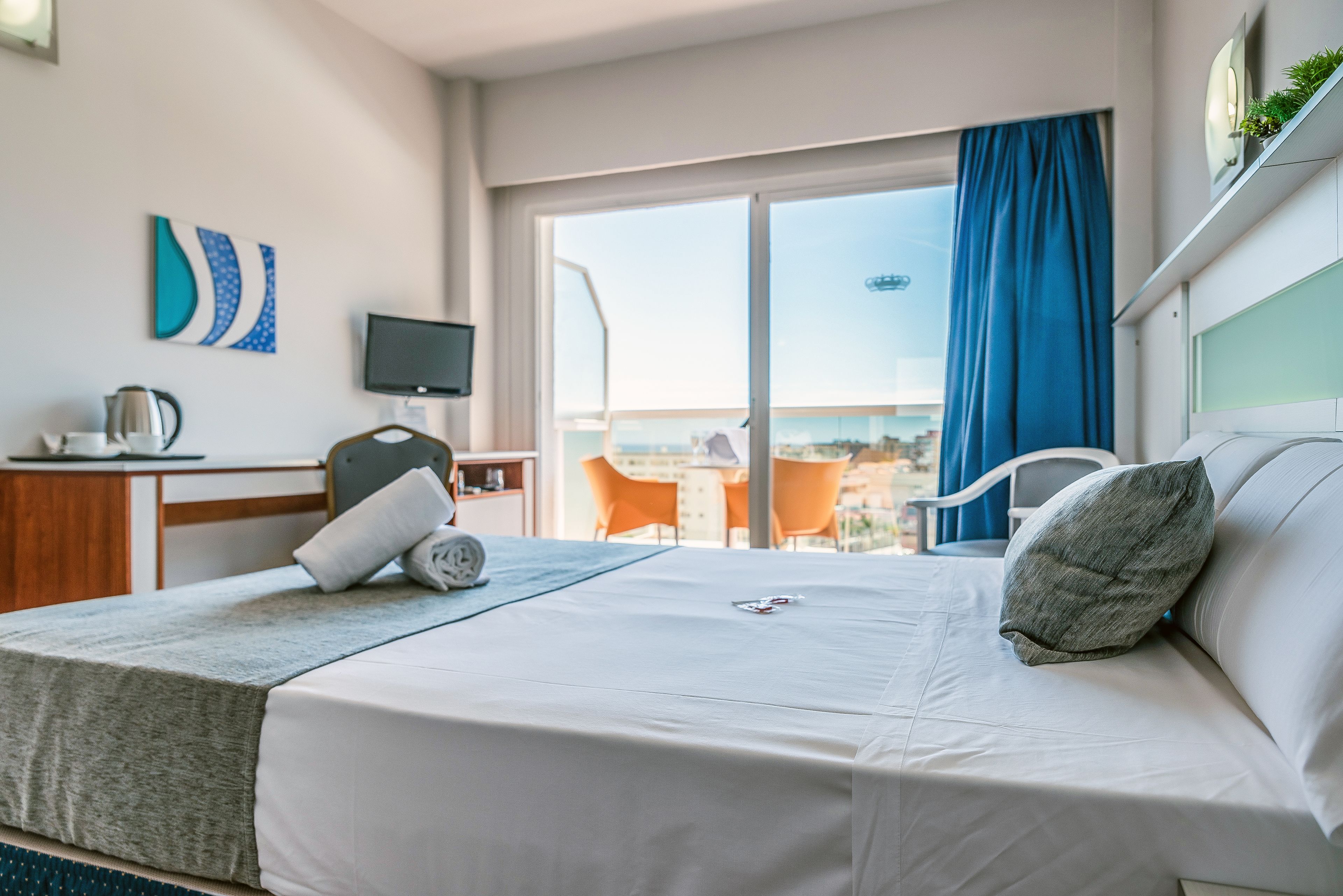 Une chambre d’hôtel comprenant un lit, un bureau avec une télévision, une fenêtre donnant sur un paysage agréable et un balcon avec des chaises.
