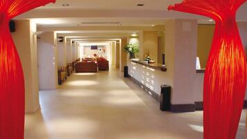 Un pasillo de hotel con mostrador de recepción, zona de estar y vista a una habitación.