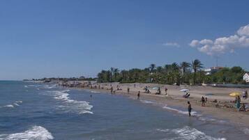 Een strand met mensen, parasols en palmbomen.