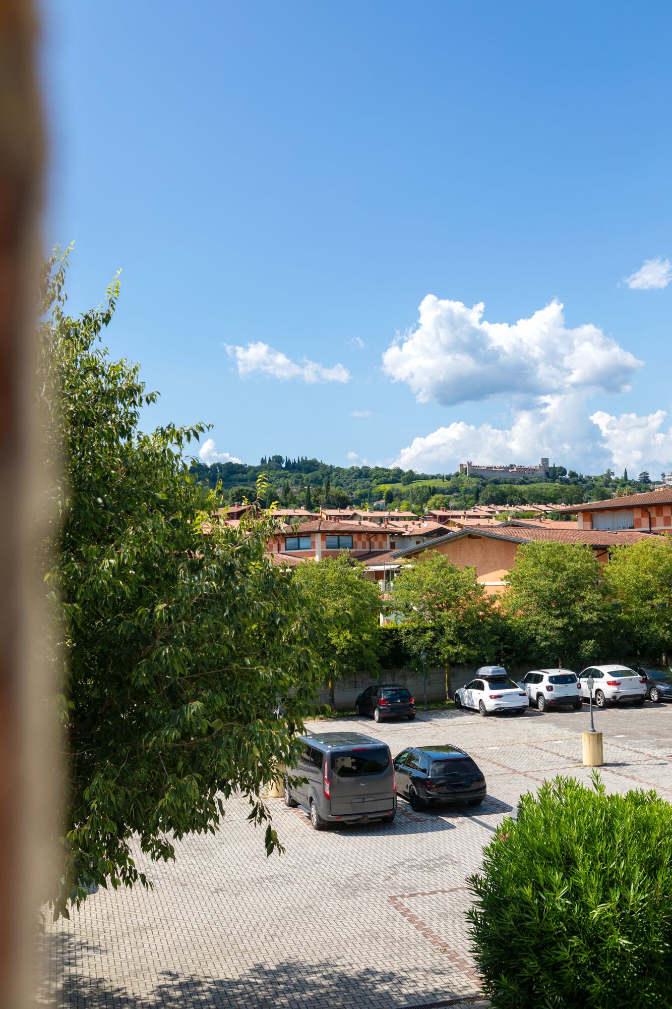 A parking area with several cars, a building with red-tiled roofs, and a castle in the background.