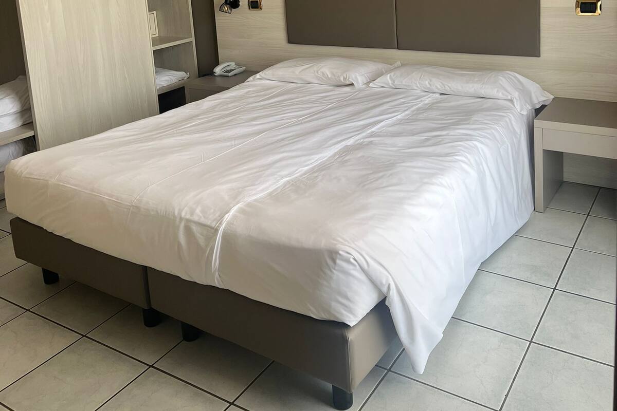 Ein modernes Hotelzimmer mit einem großen Bett, einem Kleiderschrank, einem Nachttisch mit Lampe und einem weiteren Tisch mit Telefon.