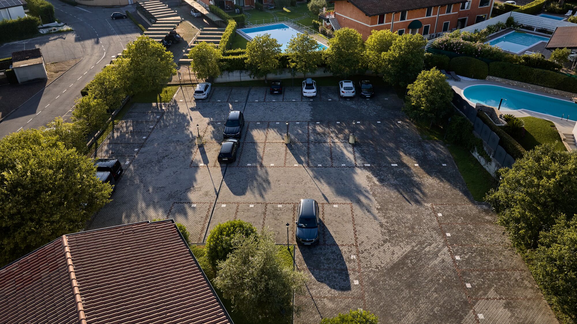 An aerial view of a parking lot with multiple cars, surrounded by trees and buildings with a swimming pool.