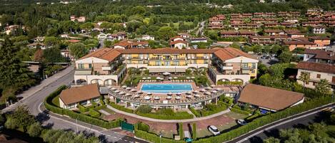 Un hotel con piscina central, varios balcones y zonas ajardinadas alrededor.