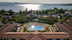Un resort con piscina central, rodeado de tumbonas y sombrillas, y vista a un lago y montañas al fondo.