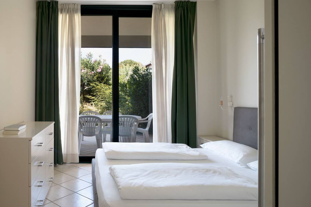 Ein Hotelzimmer mit Bett, Schreibtisch und Blick auf einen Balkon mit Stühlen.