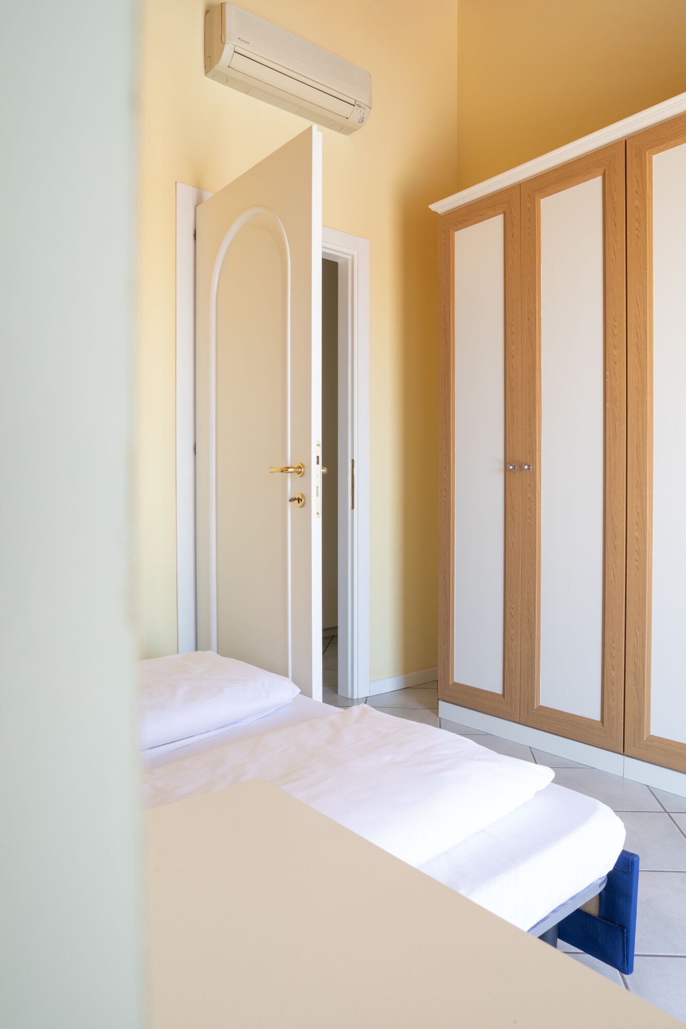 A bedroom with a bed, an air conditioning unit, a wardrobe, and a door leading to another room.