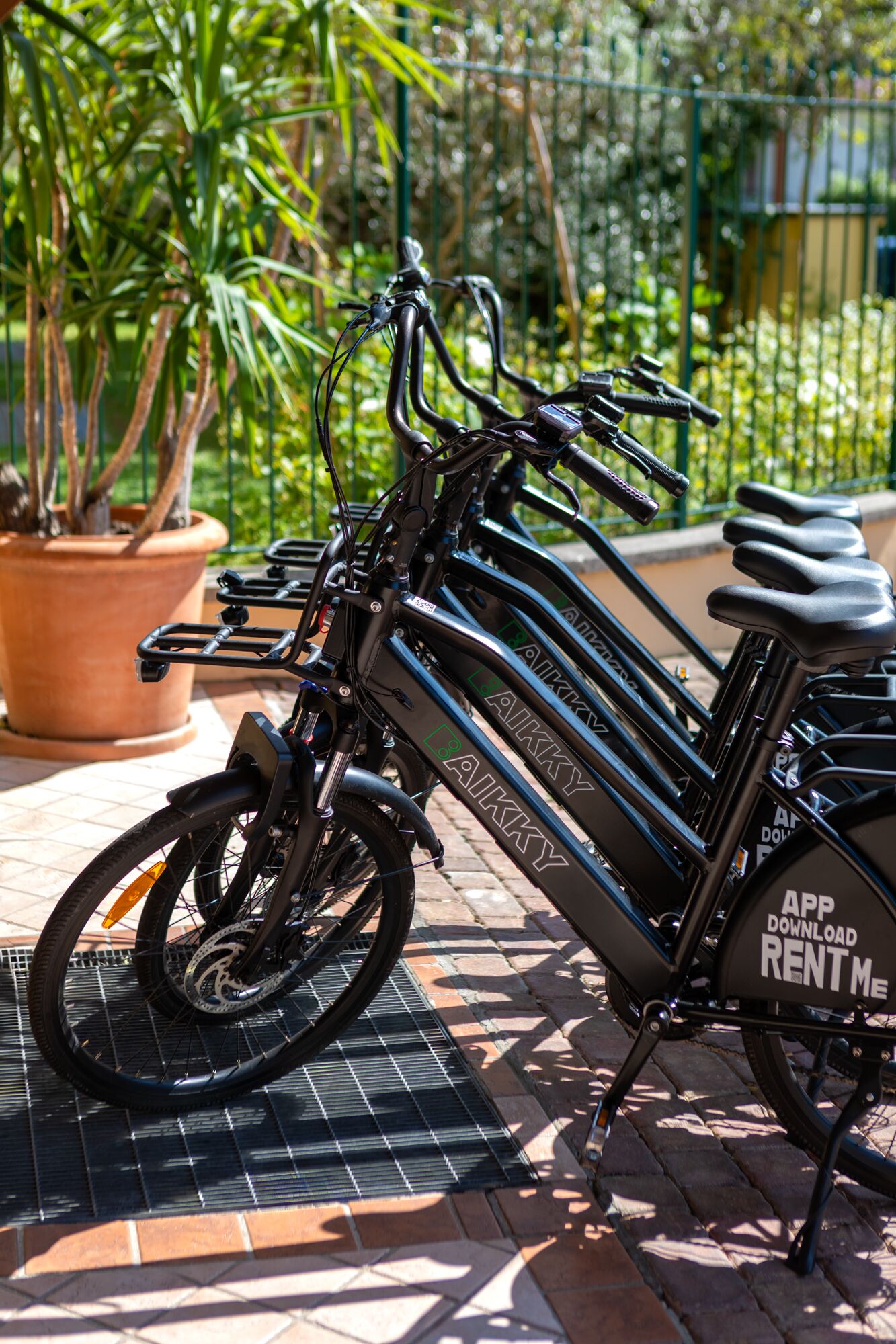 Un vélo électrique à assistance électrique, stationné sur une surface carrelée, avec une étiquette indiquant « À louer », et une plante en pot à proximité.