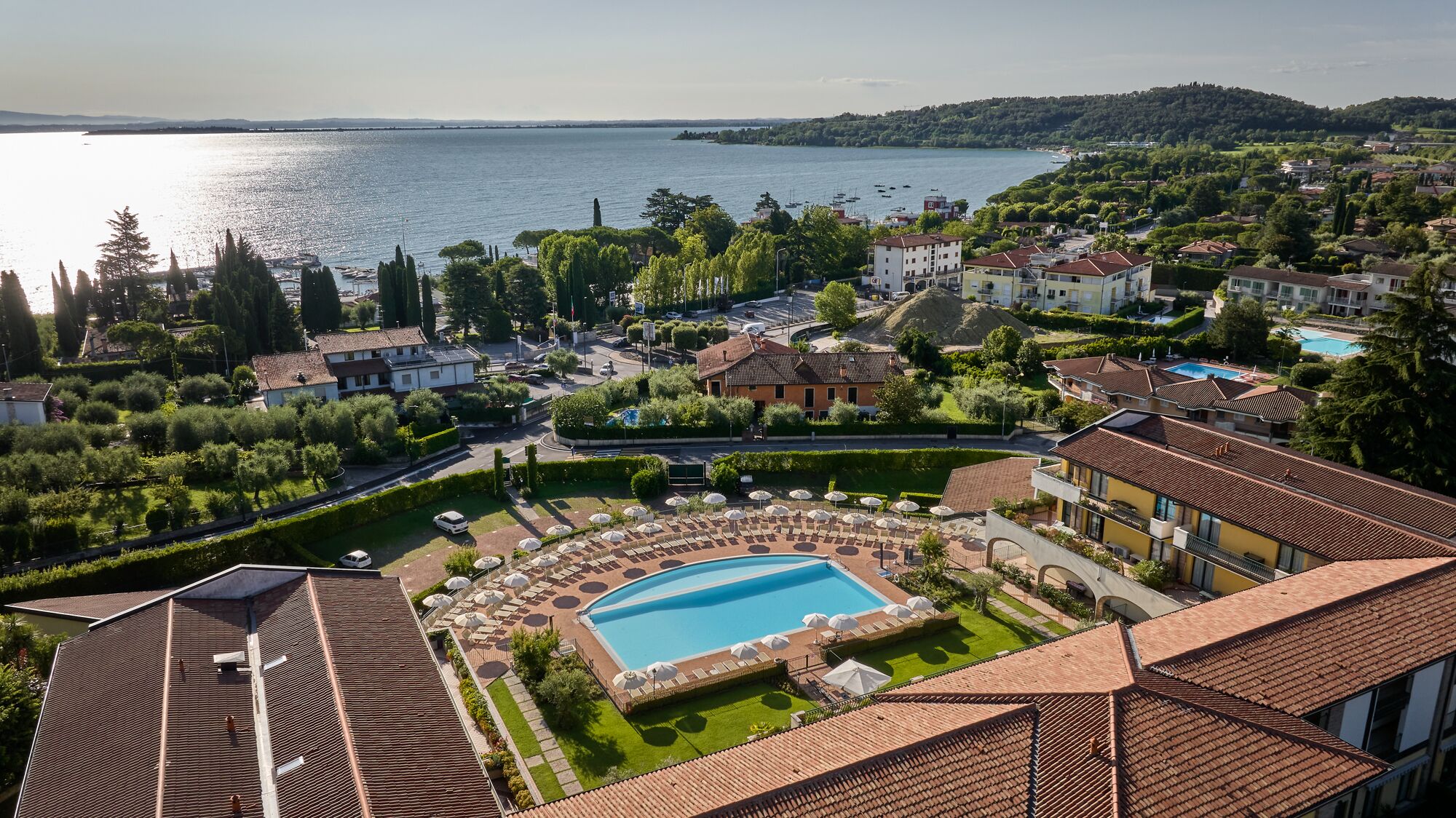 A resort with a swimming pool, surrounded by lush greenery and a view of the sea.
