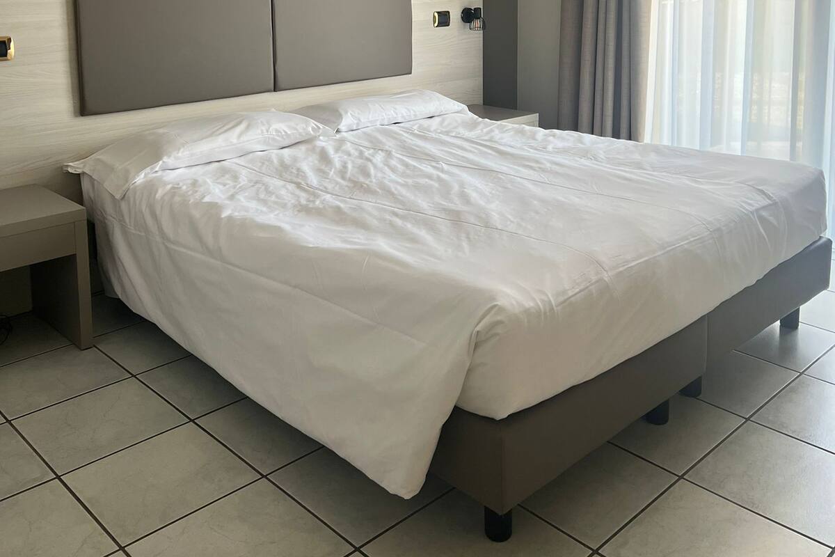 Ein modernes Hotelzimmer mit einem großen Bett, einem Nachttisch und einem Fenster mit Vorhängen.