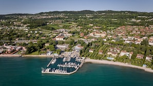 An aerial view of a coastal town with a marina, residential areas, and hilly terrain in the background.