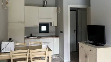 Un ambiente compatto con angolo cottura, zona pranzo e TV su un mobile.