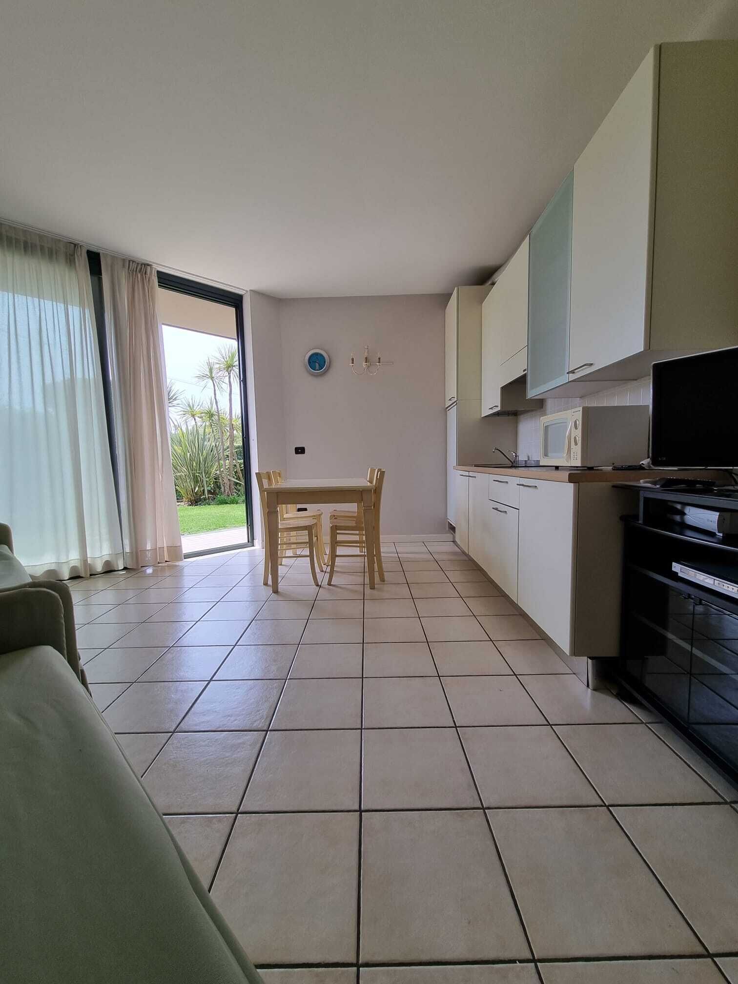 Een moderne keuken met witte kastjes, een eettafel met stoelen en een televisie.
