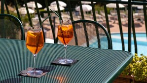 A table with two glasses of orange beverage, a metal chair, and a view of a lake and mountains.