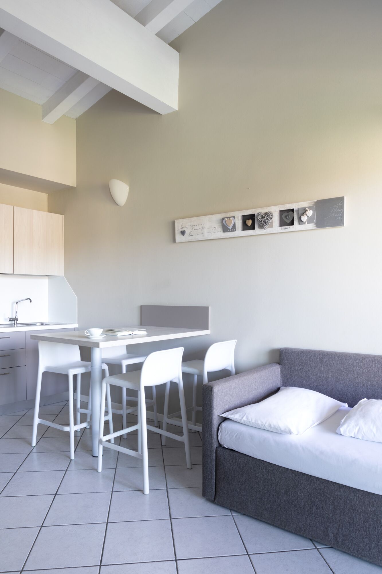 Une cuisine moderne avec des meubles blancs, une table à manger avec quatre chaises et un canapé gris avec des coussins blancs.