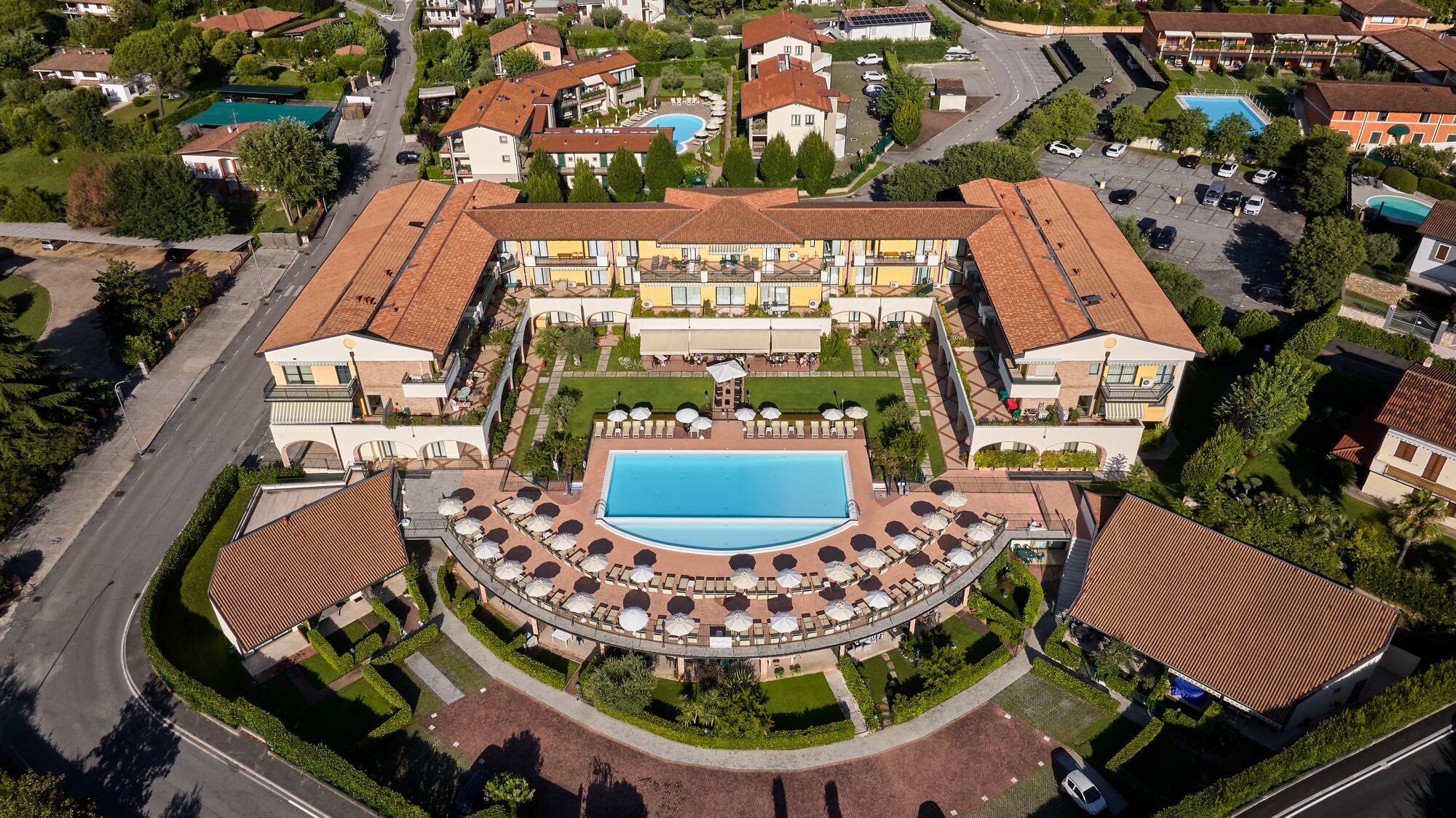 Vista aérea de un hotel con piscina central, numerosas habitaciones y un patio ajardinado.