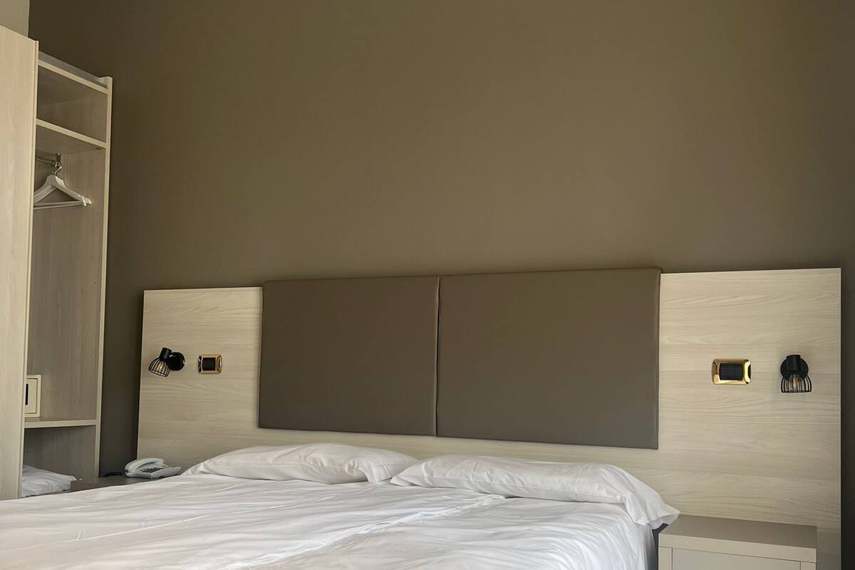Ein modernes Hotelzimmer mit einem großen Bett, einem Nachttisch, einem Kleiderschrank und einer Wandlampe.