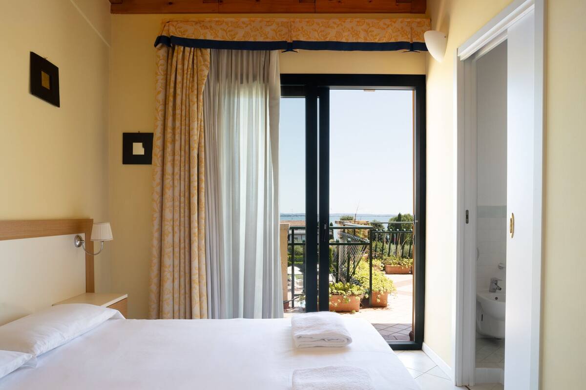 Ein Hotelzimmer mit einem großen Bett, Blick auf einen Balkon und einer Tür zu einem Badezimmer.