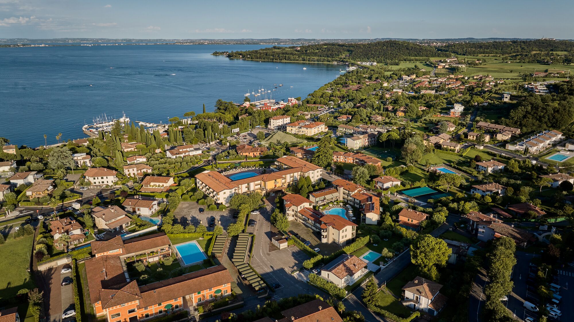 Ett flygbildsfoto av ett bostadsområde vid kusten med hus, en småbåtshamn och en stor vattenyta.