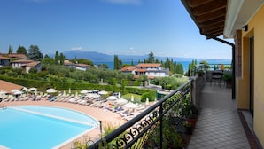A balcony with a pool, lounge chairs, and a view of a mountain and lake.