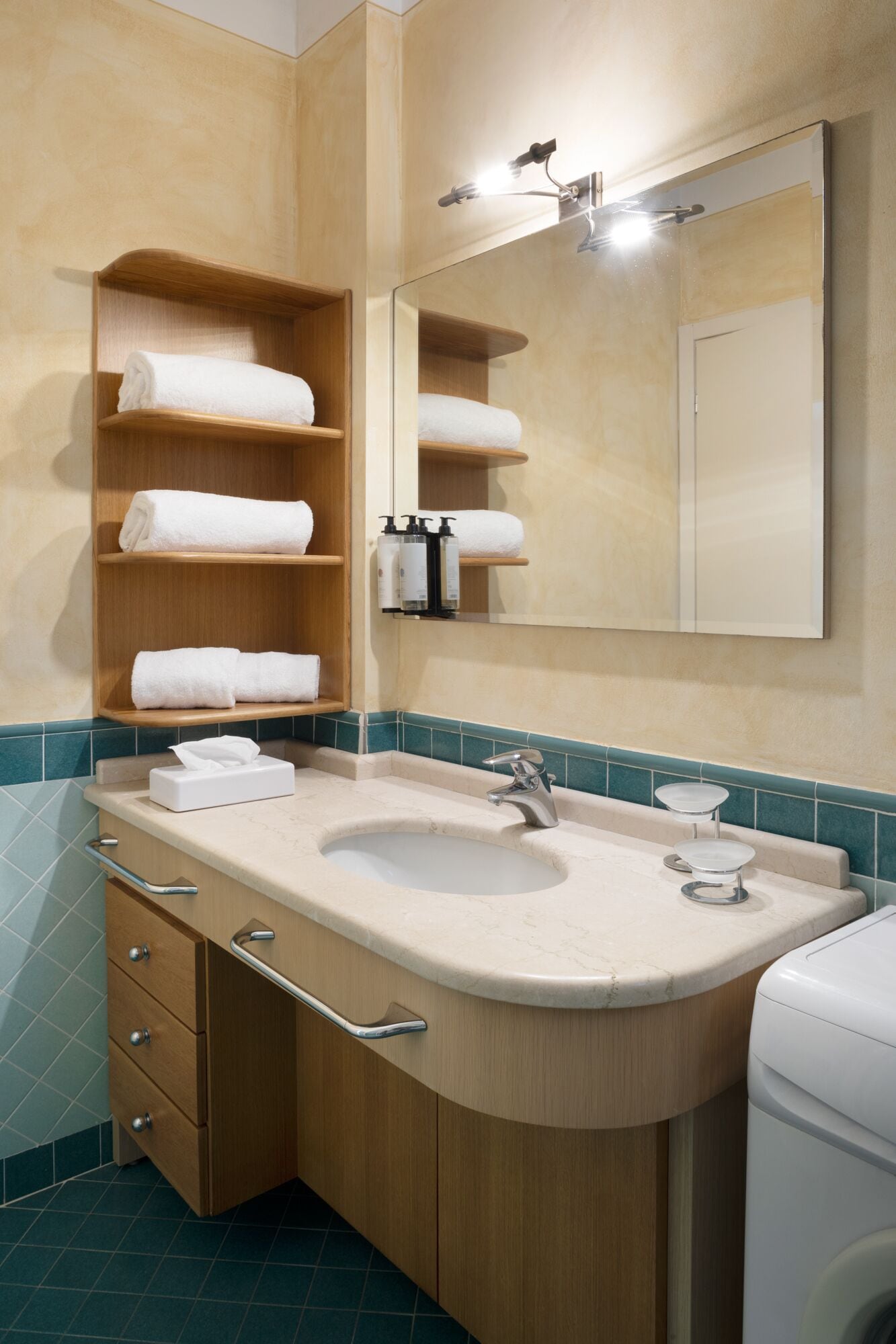 Un baño con tocador de madera, lavamanos, espejo y repisas con toallas.