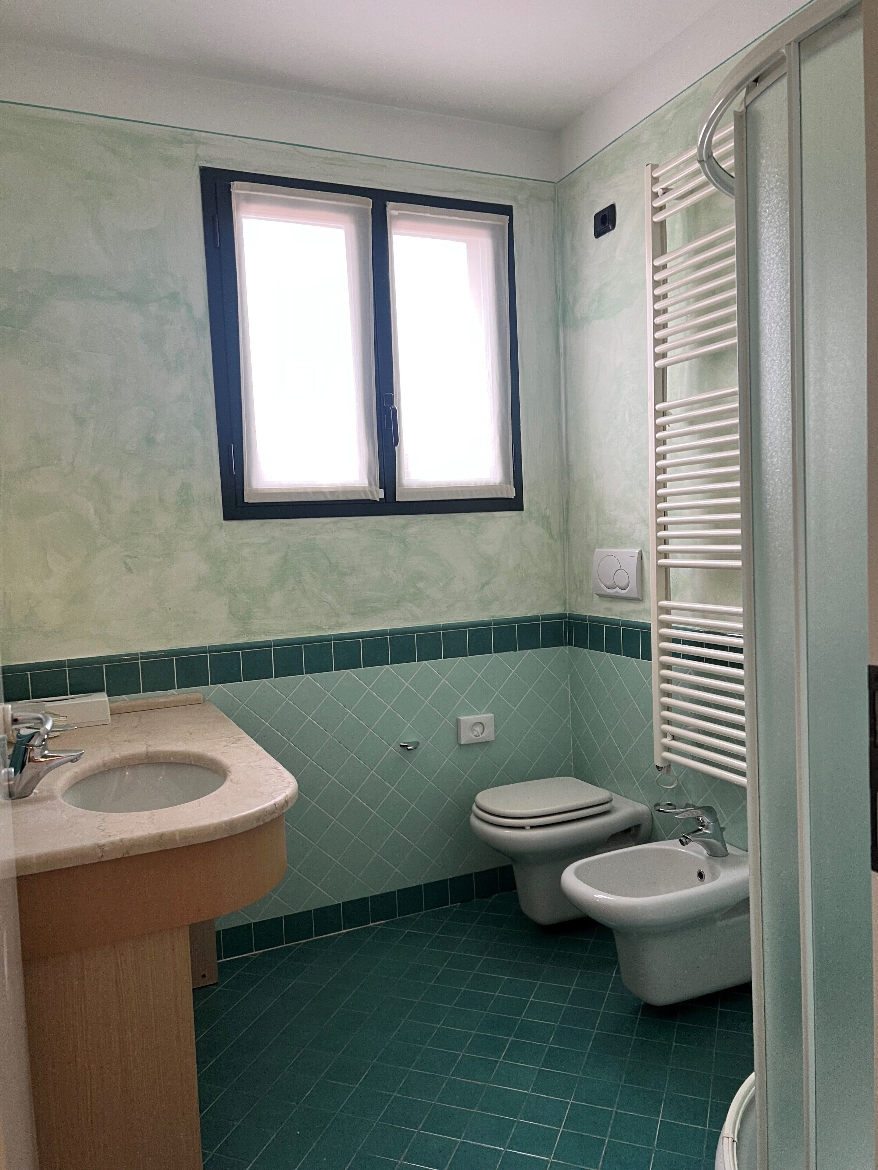 A bathroom with a sink, toilet, bidet, and a window with blinds.