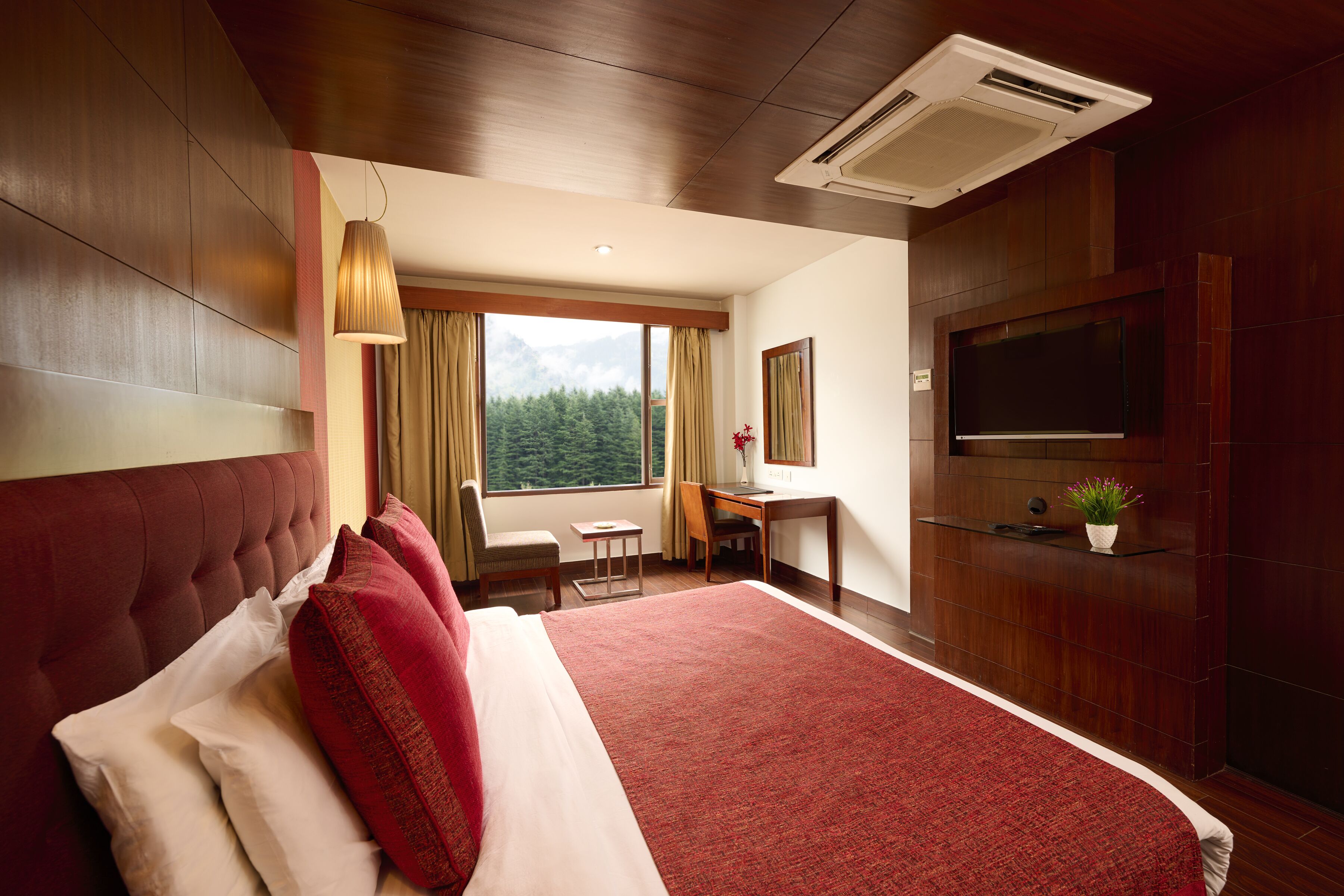 A hotel room with a large bed, a desk, a chair, a TV, and a window with a view of the mountains.