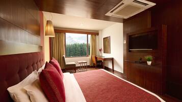 A hotel room with a large bed, a desk, a chair, a TV, and a window with a view of the mountains.