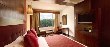 Hotelkamer met een groot bed, een bureau, een stoel, een televisie en een raam met uitzicht op de bergen.